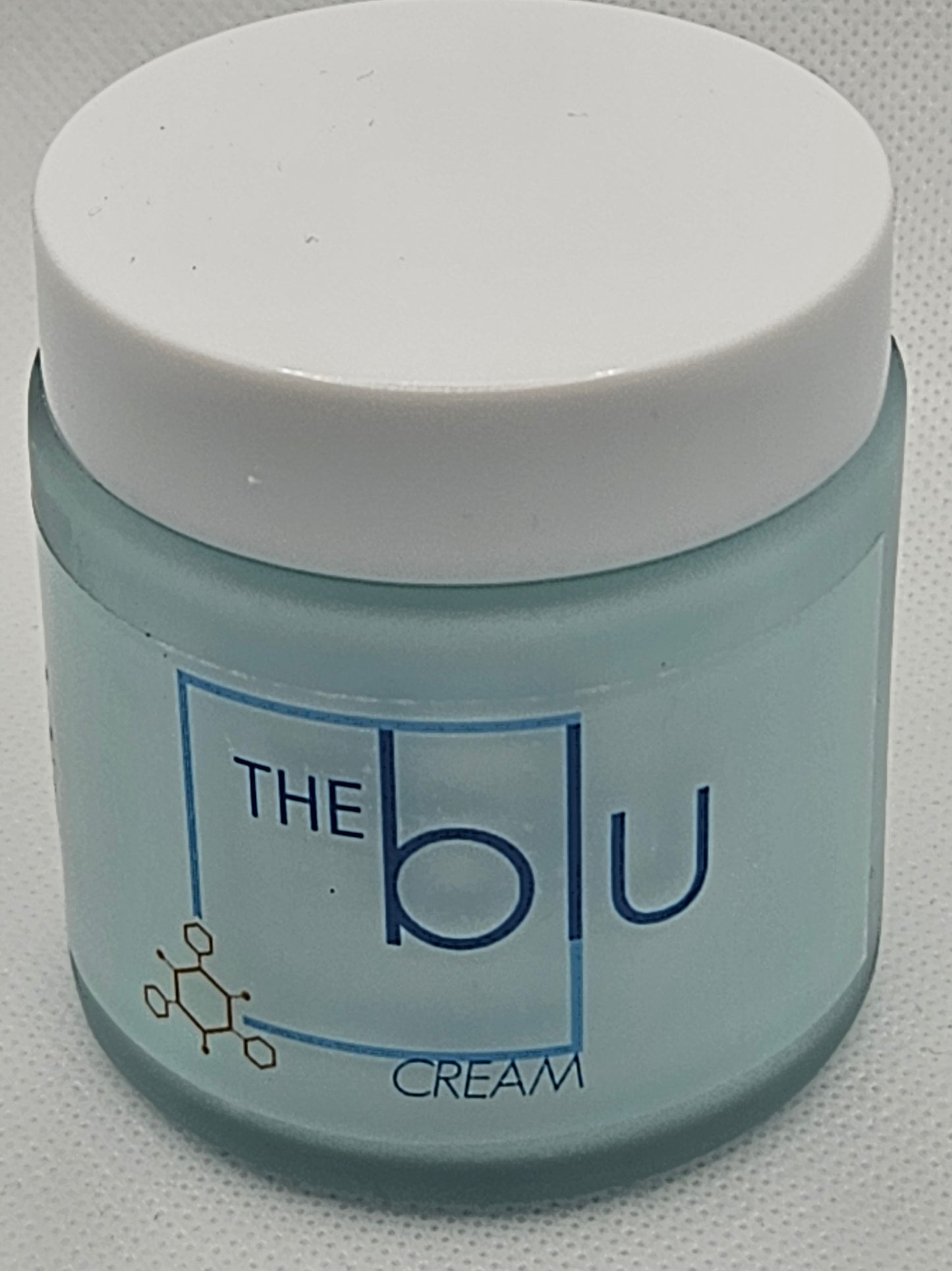 A small frosted glass jar with a white lid labeled The Blu Cream - Zinc, Copper, and Magnesium in blue text, featuring a honeycomb design—this mineral cream soothes damaged skin.