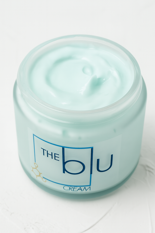 An open jar of The Blu Cream - Zinc, Copper, and Magnesium sits on a white surface. Its smooth, whipped texture soothes damaged skin, and the frosted glass jar is adorned with blue and gold labeling.