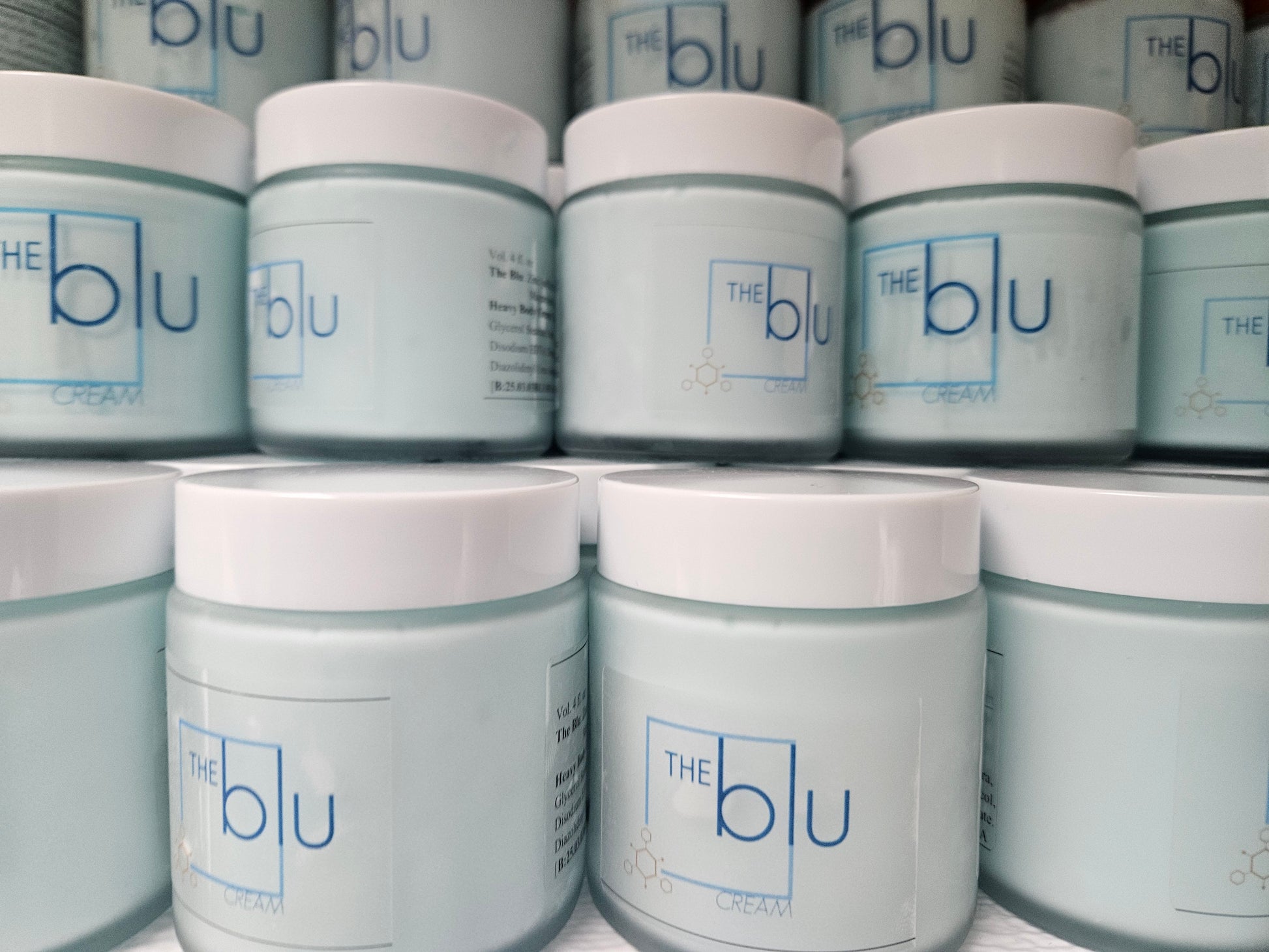 Several stacked light blue jars with white lids, labeled The Blu Cream - Zinc, Copper, and Magnesium in blue text, are closely arranged—this premium mineral cream is designed to soothe damaged skin.