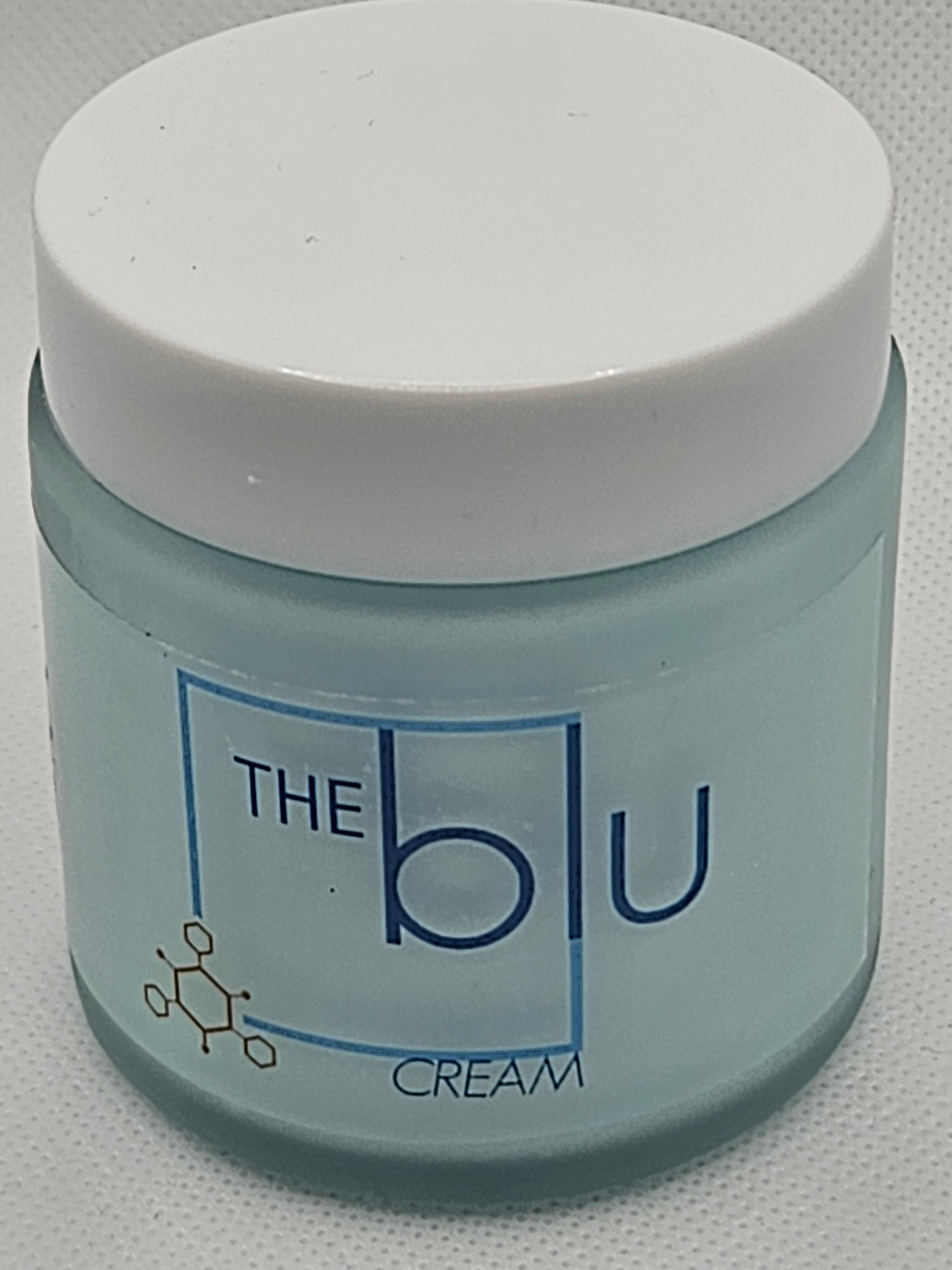 A small frosted glass jar with a white lid labeled The Blu Cream - Zinc, Copper, and Magnesium in blue text, featuring a honeycomb design—this mineral cream soothes damaged skin.